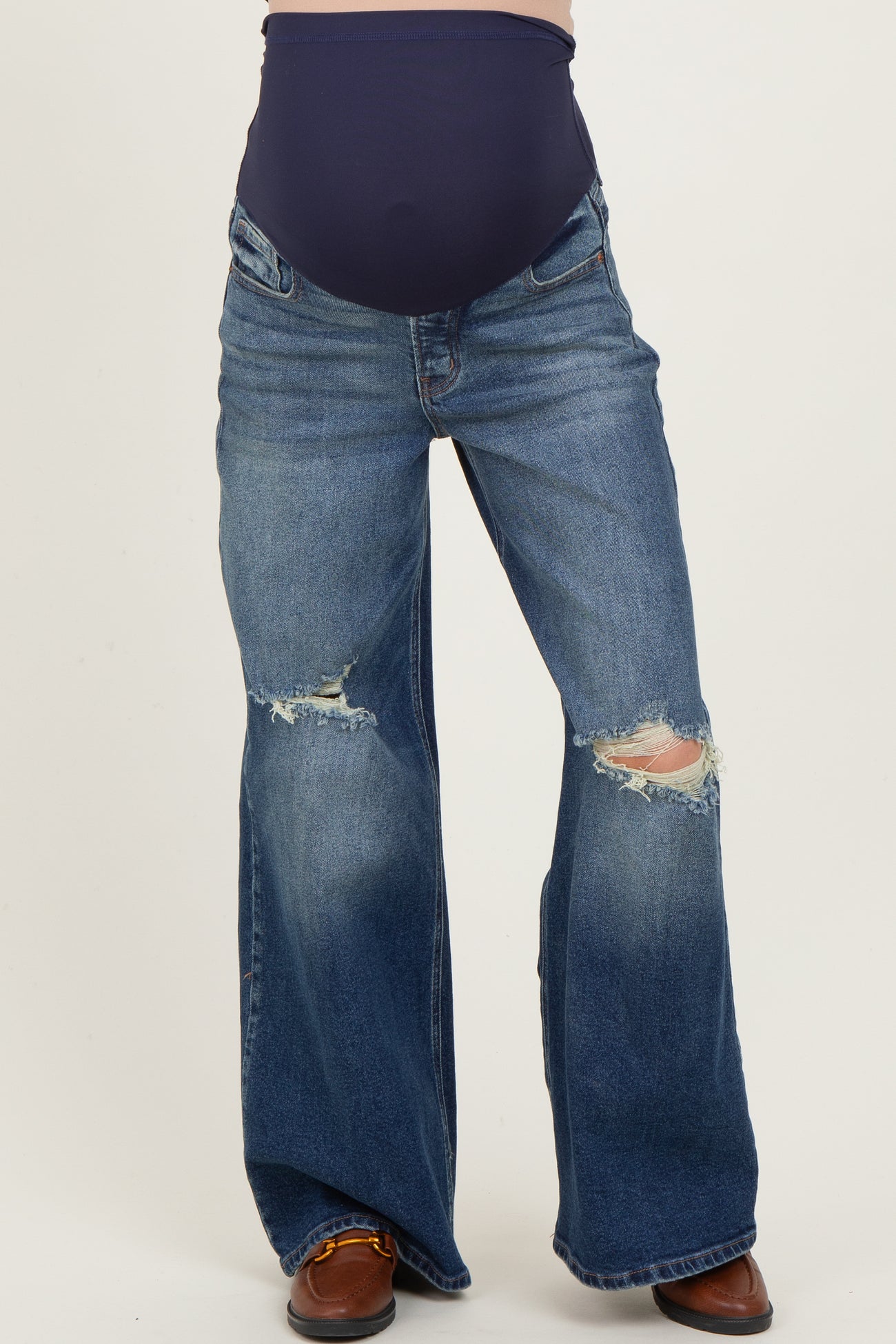 maternity wear dark blue belly support flared jeans with distressed details, worn by a model showcasing a baby bump