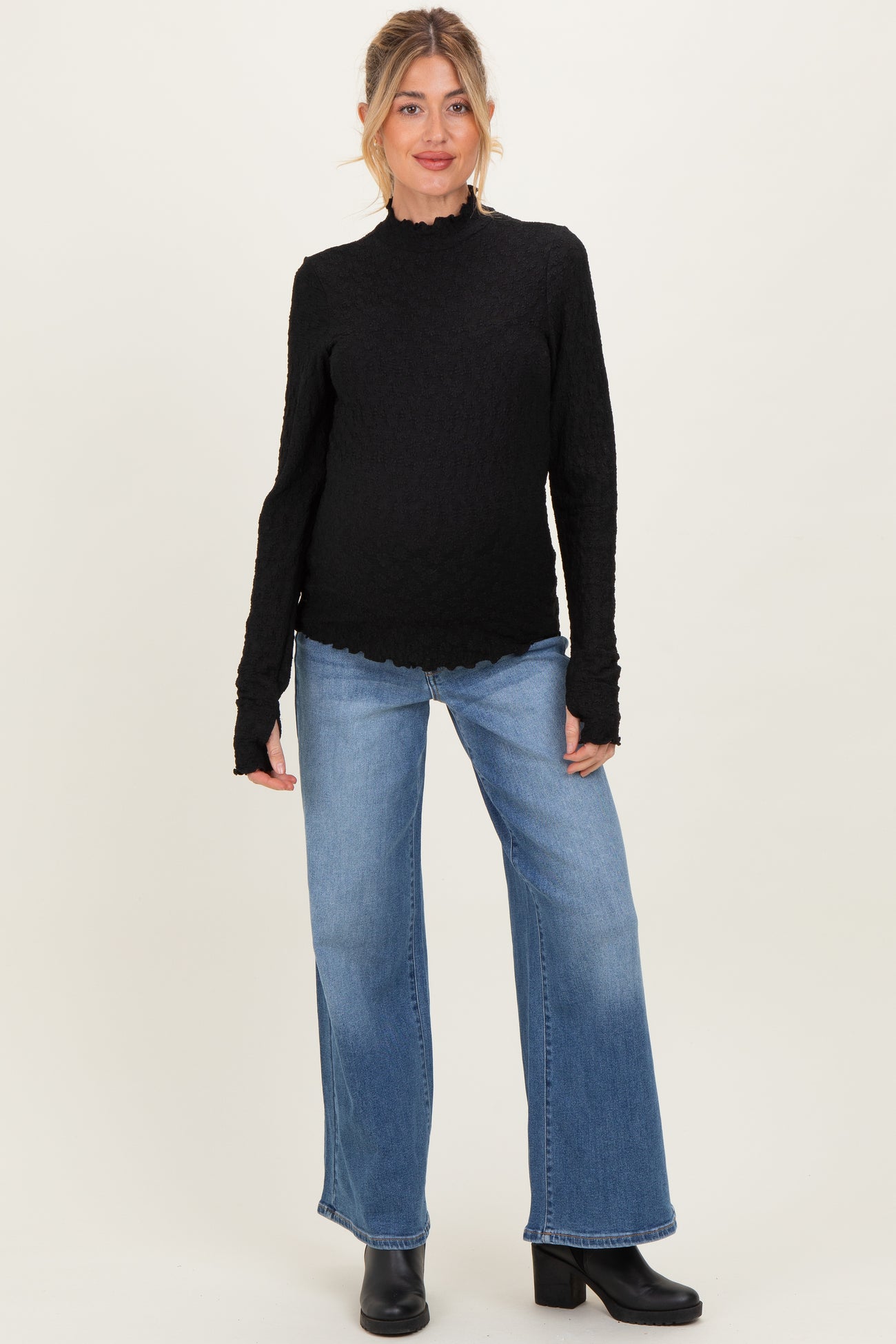 woman wearing a black long sleeve maternity top with ruffle details and blue wide-leg jeans, showing her baby bump
