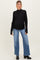 woman wearing a black long sleeve maternity top with ruffle details and blue wide-leg jeans, showing her baby bump