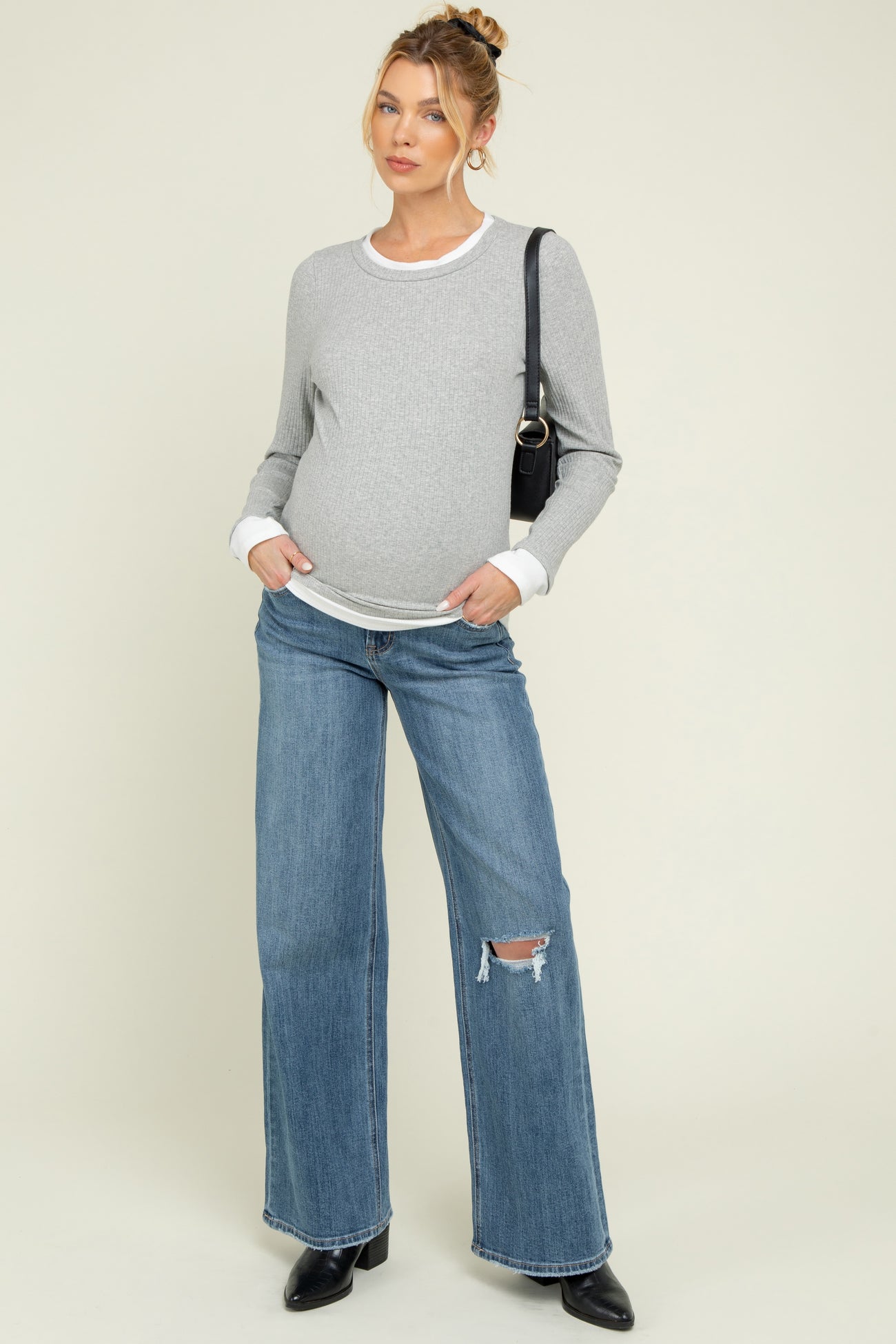 woman wearing a gray maternity long sleeve sweater and distressed wide-leg jeans, showing her baby bump