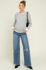 woman wearing a gray maternity long sleeve sweater and distressed wide-leg jeans, showing her baby bump