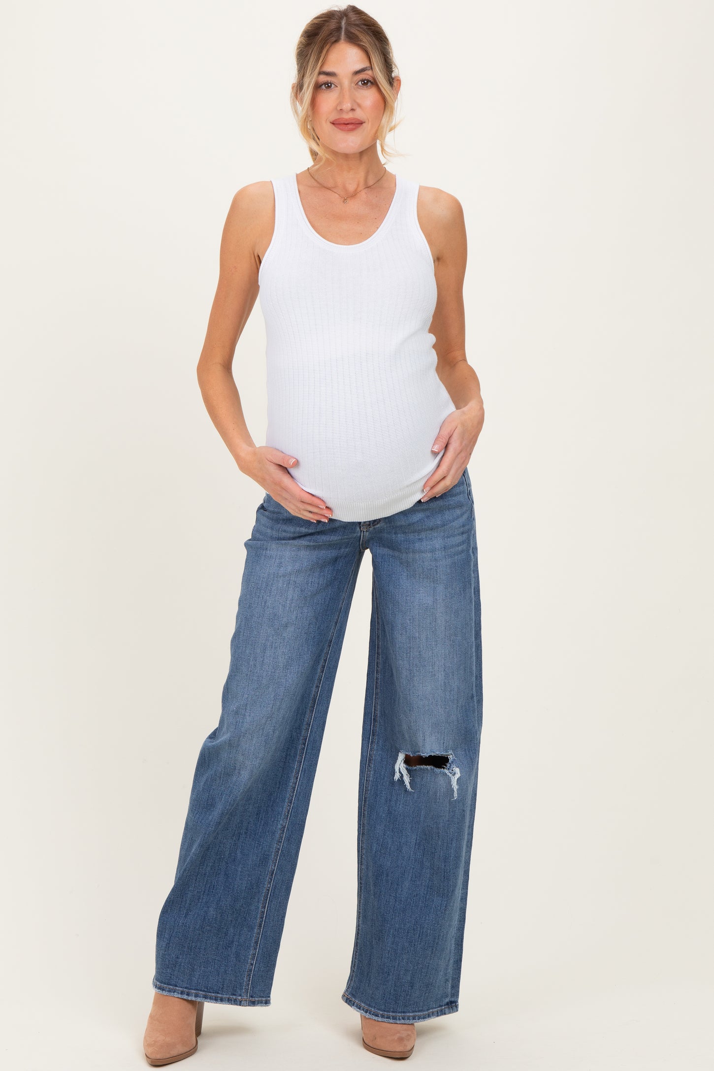 woman wearing a white ribbed tank top and distressed wide-leg maternity jeans, showcasing her baby bump