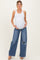 woman wearing a white ribbed tank top and distressed wide-leg maternity jeans, showcasing her baby bump