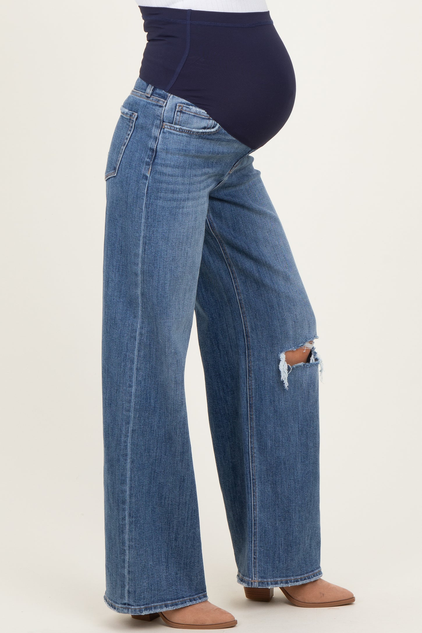 woman wearing light blue distressed maternity jeans with a dark blue over-the-bump waistband and a visible baby bump