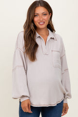 woman wearing a light beige maternity sweater with a front pocket and oversized fit, showing her baby bump