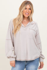 woman wearing a light beige oversized pullover top with a collar and front pocket, paired with blue jeans