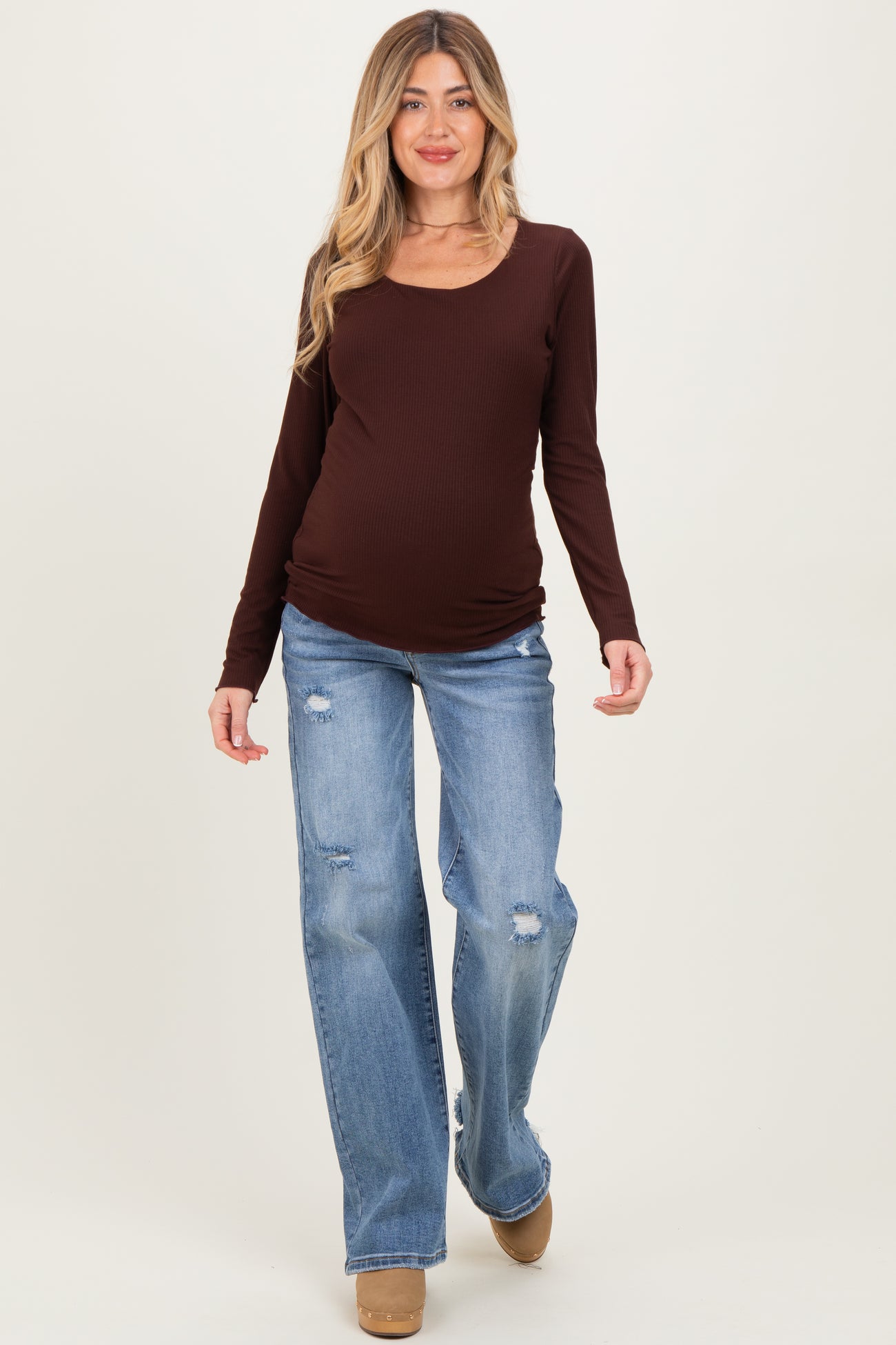 woman wearing a brown long sleeve maternity top and distressed light blue jeans, showcasing her baby bump
