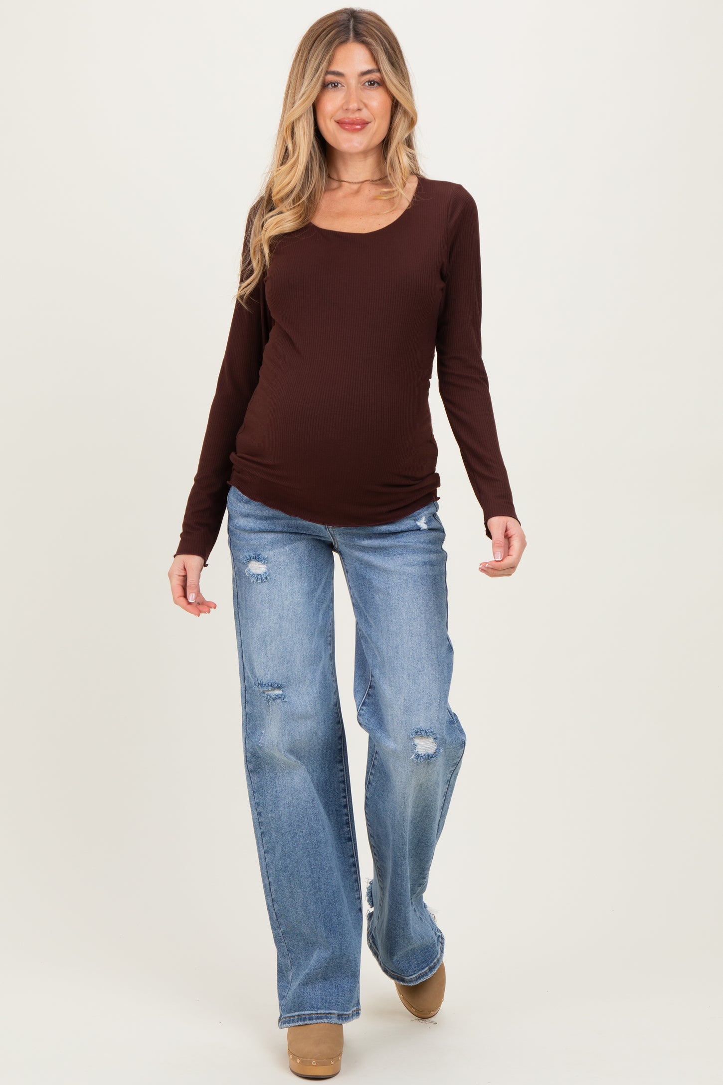 woman wearing a brown long sleeve maternity top and distressed light blue jeans, showcasing her baby bump