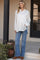 woman wearing a white satin maternity shirt and blue flared jeans, showcasing her baby bump while standing outdoors