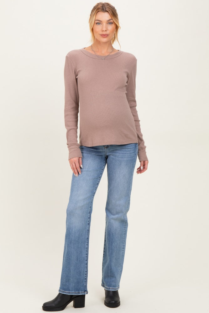 woman wearing a taupe long sleeve maternity top and blue flared jeans, showing her baby bump