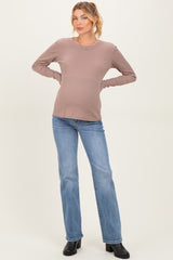 woman wearing a light brown long sleeve maternity top and blue flared jeans, showing her baby bump