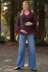 woman wearing a burgundy and gray striped maternity sweater and blue wide-leg jeans, holding her baby bump