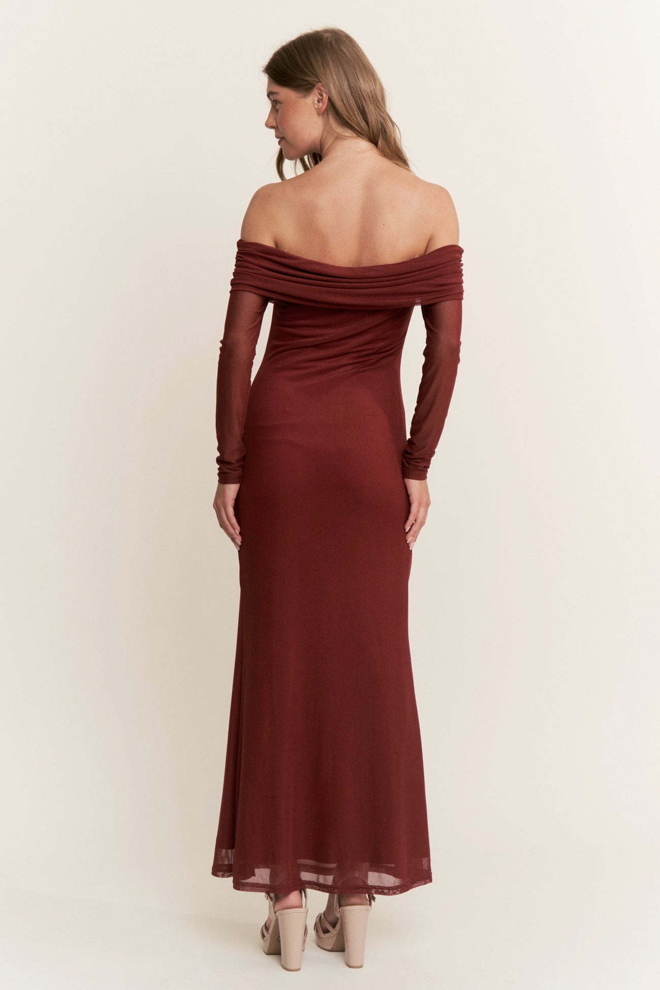 woman wearing a burgundy off-the-shoulder maxi dress with long sleeves, showing a fitted silhouette from the back