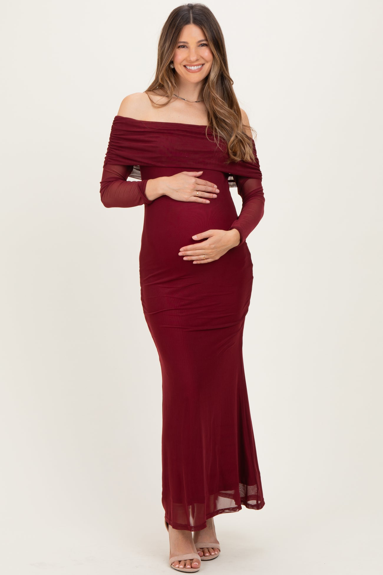 woman wearing a burgundy off-shoulder maternity dress with long sleeves and holding her baby bump