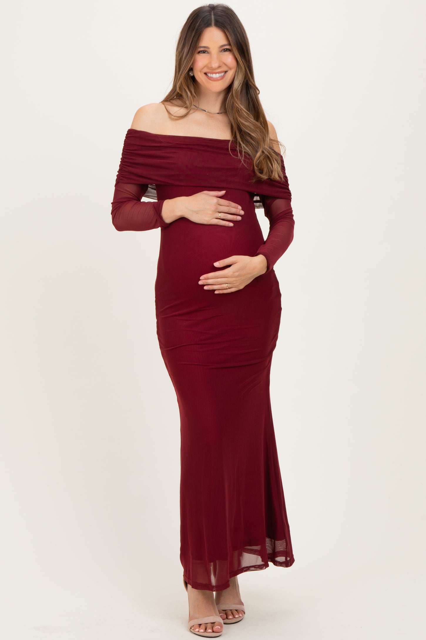 woman wearing a burgundy off-shoulder maternity dress with long sleeves and holding her baby bump