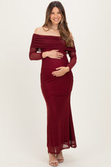 woman wearing a burgundy off-shoulder maternity dress with long sleeves and holding her baby bump