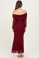 woman wearing a burgundy off-the-shoulder maternity dress with long sleeves and a flowy skirt, showing her back