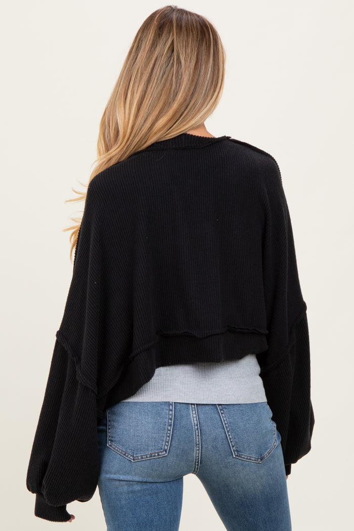 woman wearing a black cropped maternity sweater with wide sleeves, seen from the back, paired with blue jeans