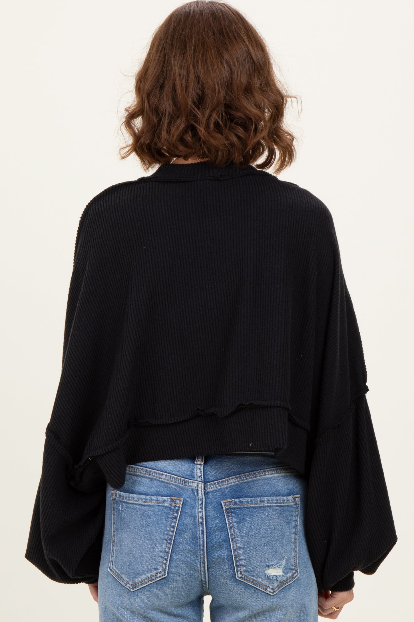 woman wearing a black oversized ribbed sweater with voluminous sleeves and a cropped back, styled with blue jeans
