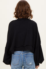 woman wearing a black oversized ribbed sweater with voluminous sleeves and a cropped back, styled with blue jeans