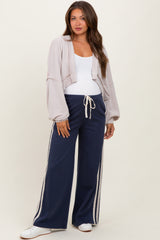 woman wearing a cropped light gray cardigan and navy maternity pants with white side stripes and drawstring