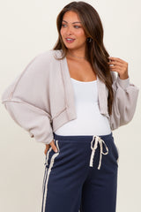 woman wearing a light taupe cropped ribbed maternity cardigan over a white tank top and paired with navy sweatpants