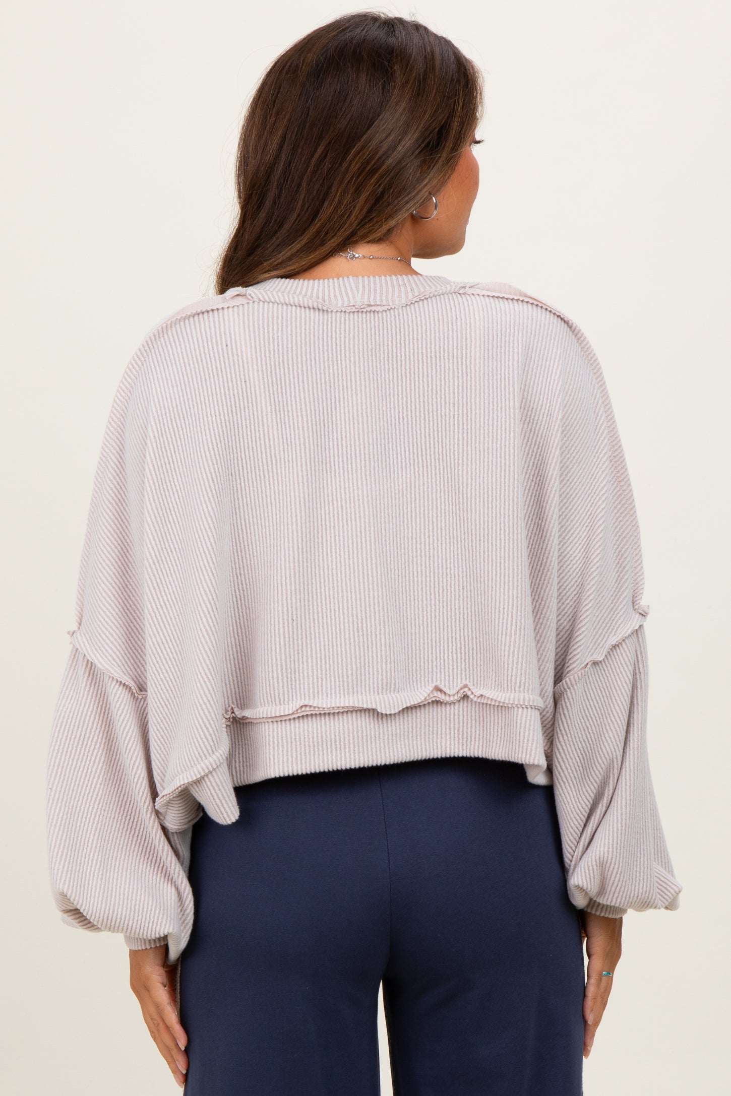 woman wearing a light pink cropped maternity sweatshirt with oversized sleeves and a ribbed texture, showing her back
