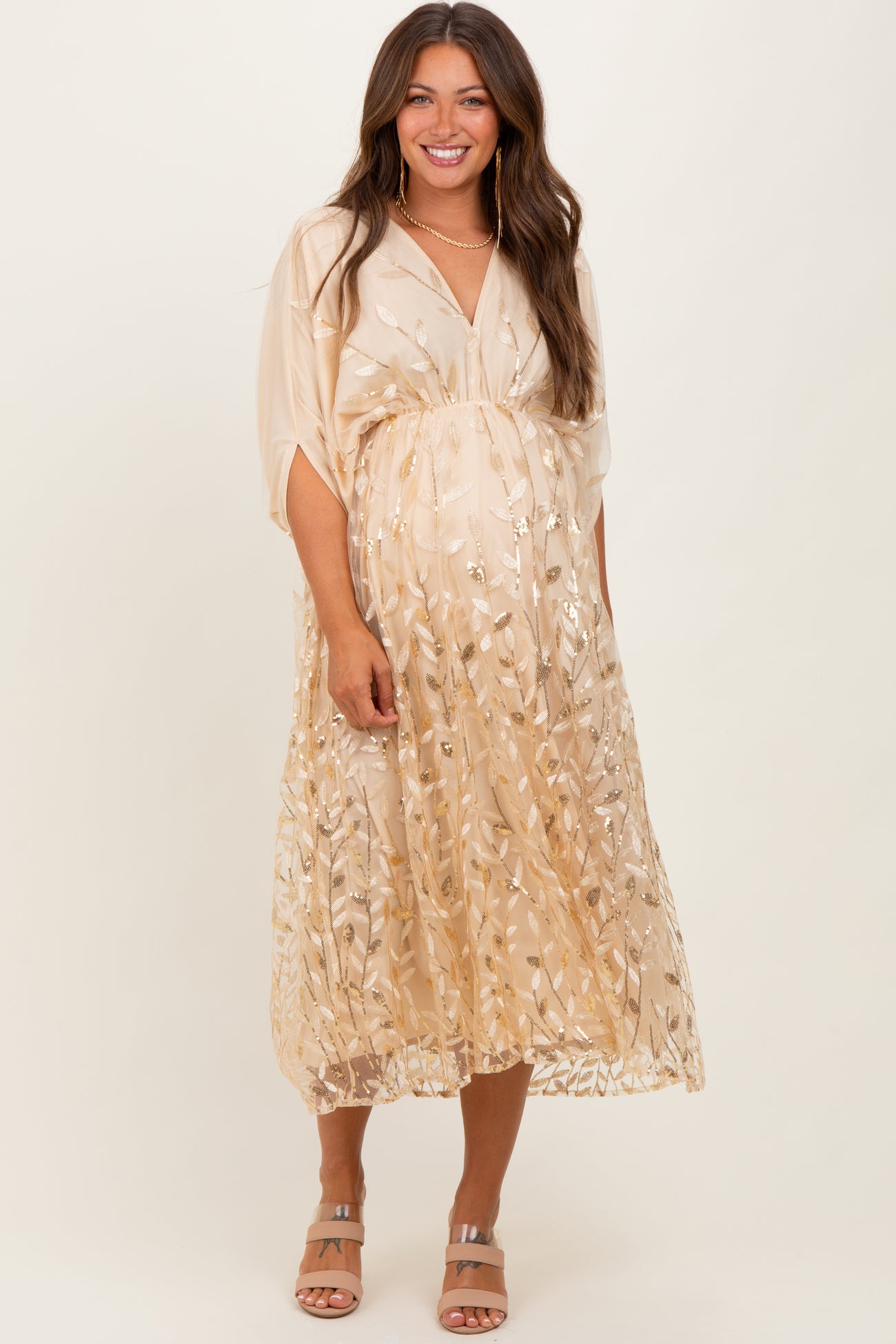 woman wearing a gold floral embroidered maternity dress with a flowing silhouette and a visible baby bump