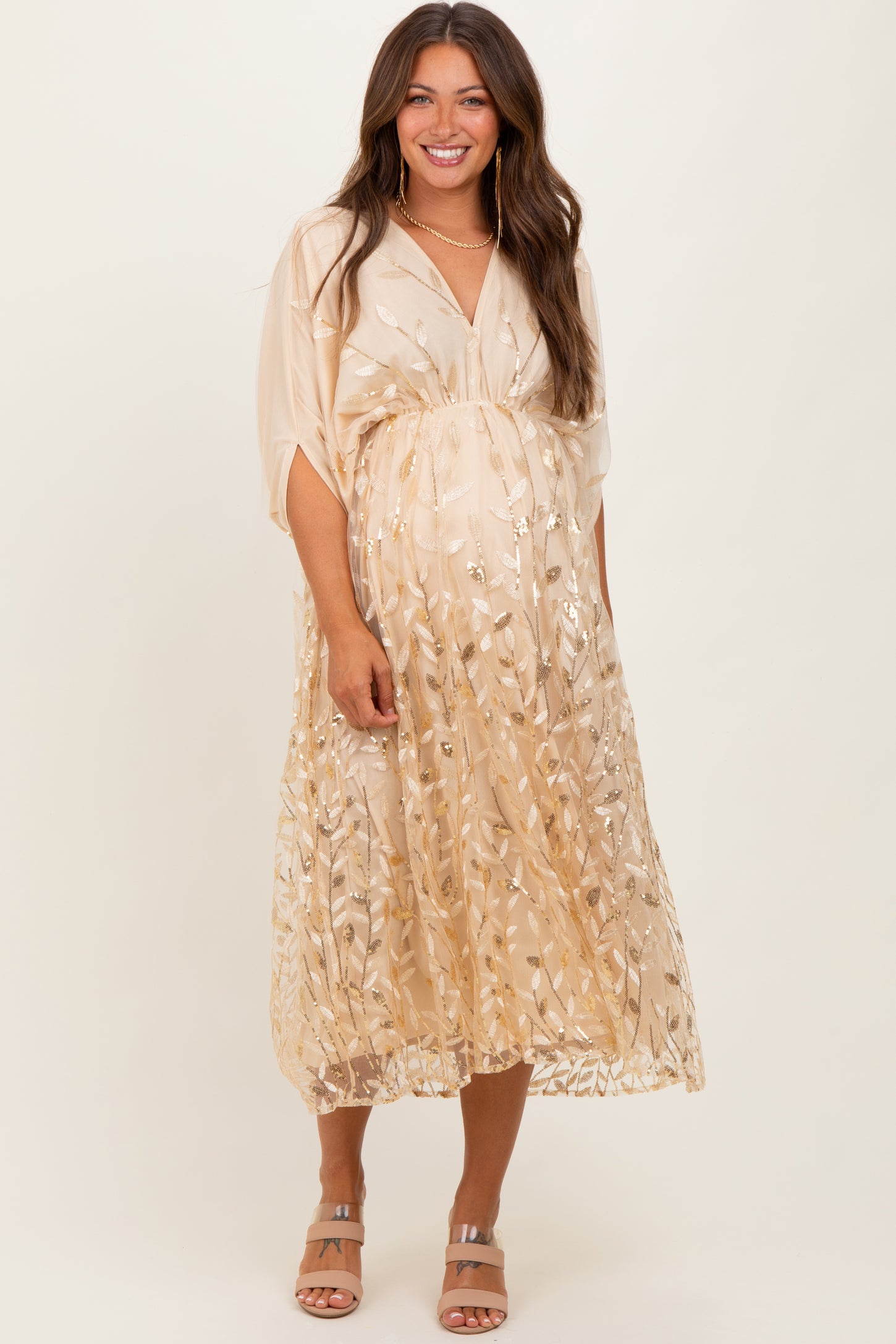 woman wearing a gold floral embroidered maternity dress with a flowing silhouette and a visible baby bump