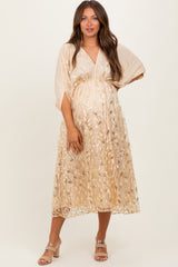 woman wearing a light beige maternity dress with a floral design and sheer sleeves, showcasing her baby bump