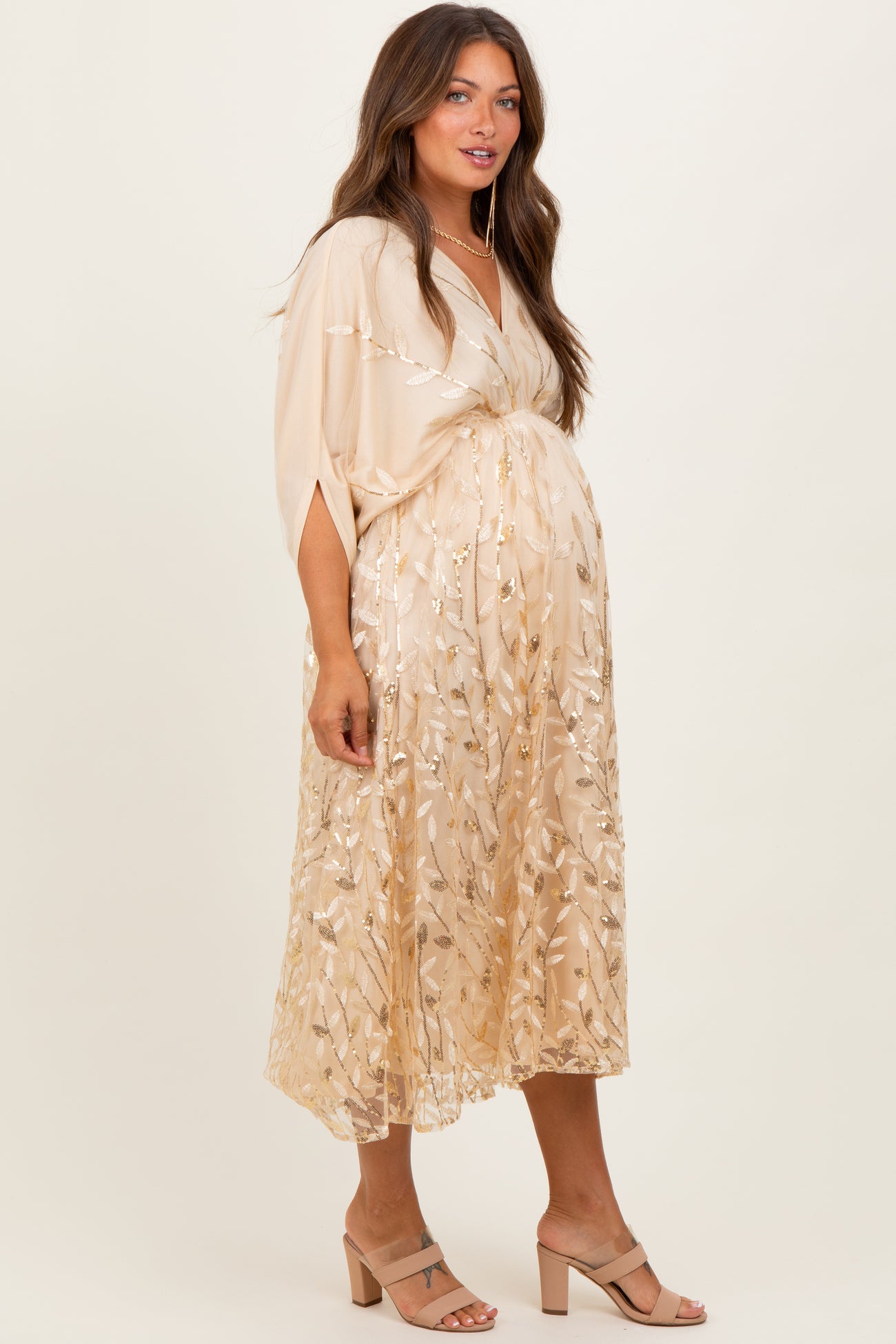 woman wearing a gold embroidered maternity dress with a flowing skirt and a plunging neckline, showcasing her baby bump
