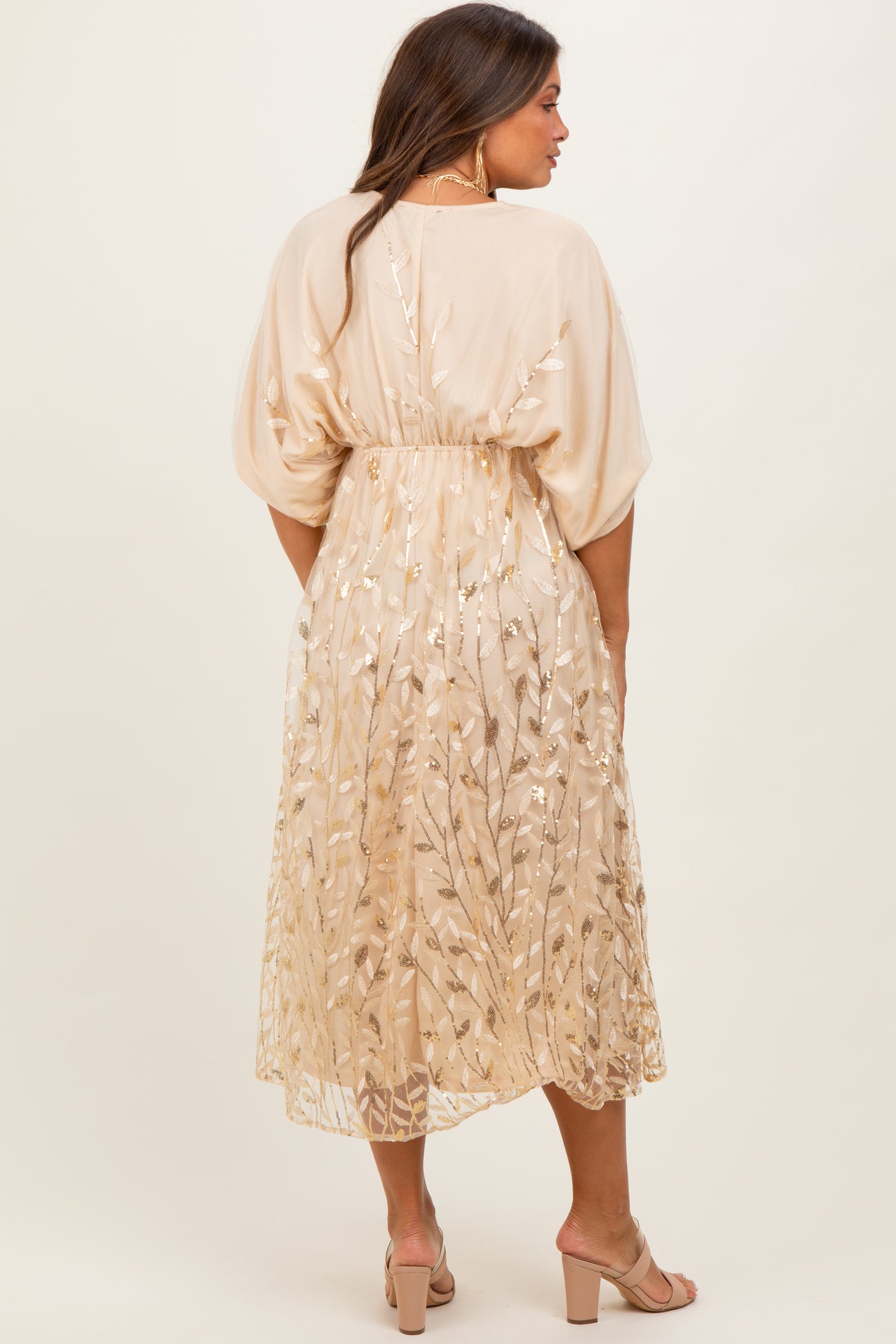 woman wearing a beige maternity dress with floral embroidery and a cinched waist, showing a baby bump from the back