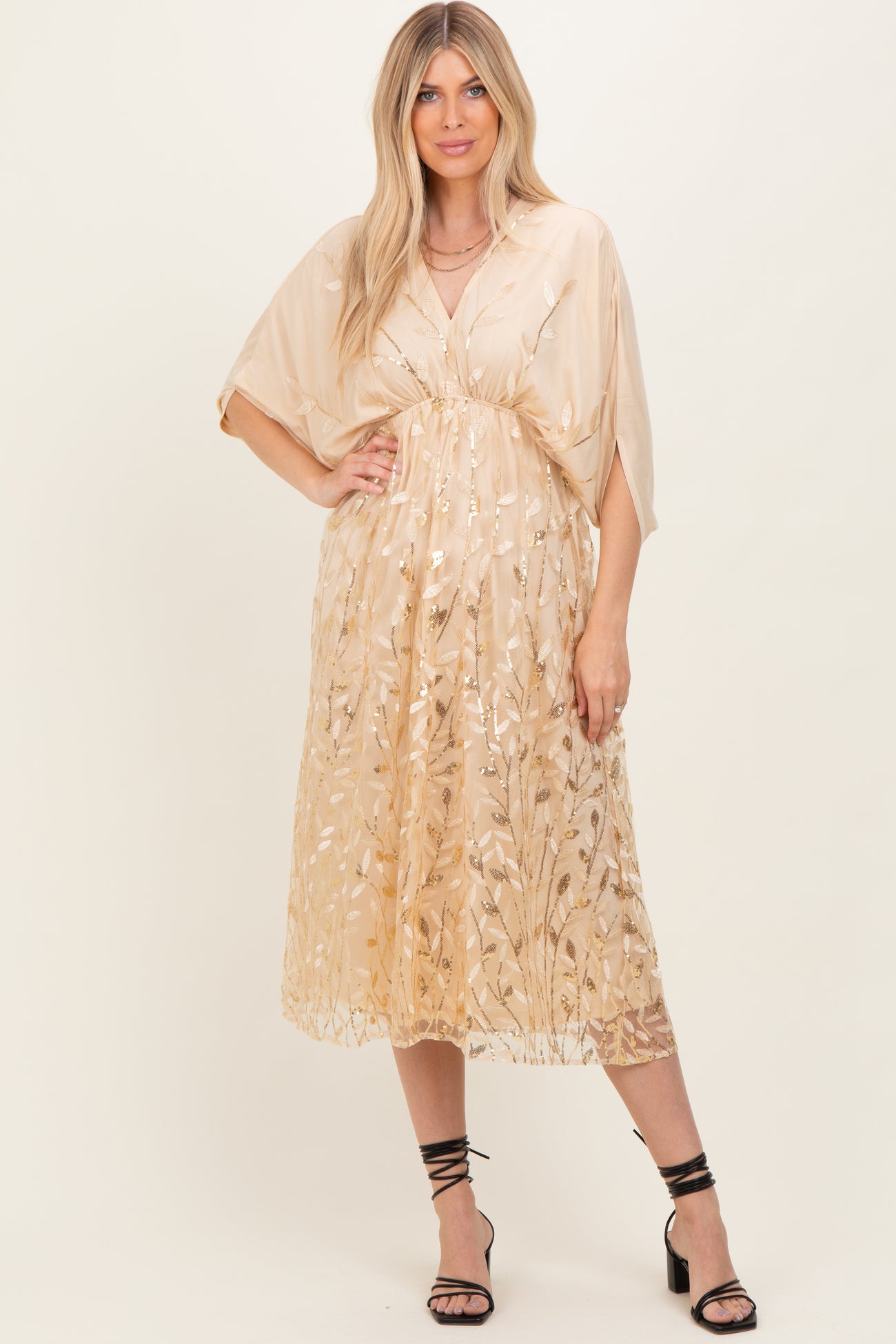 woman wearing a beige midi dress with floral sequin details and short kimono sleeves, styled with strappy black heels