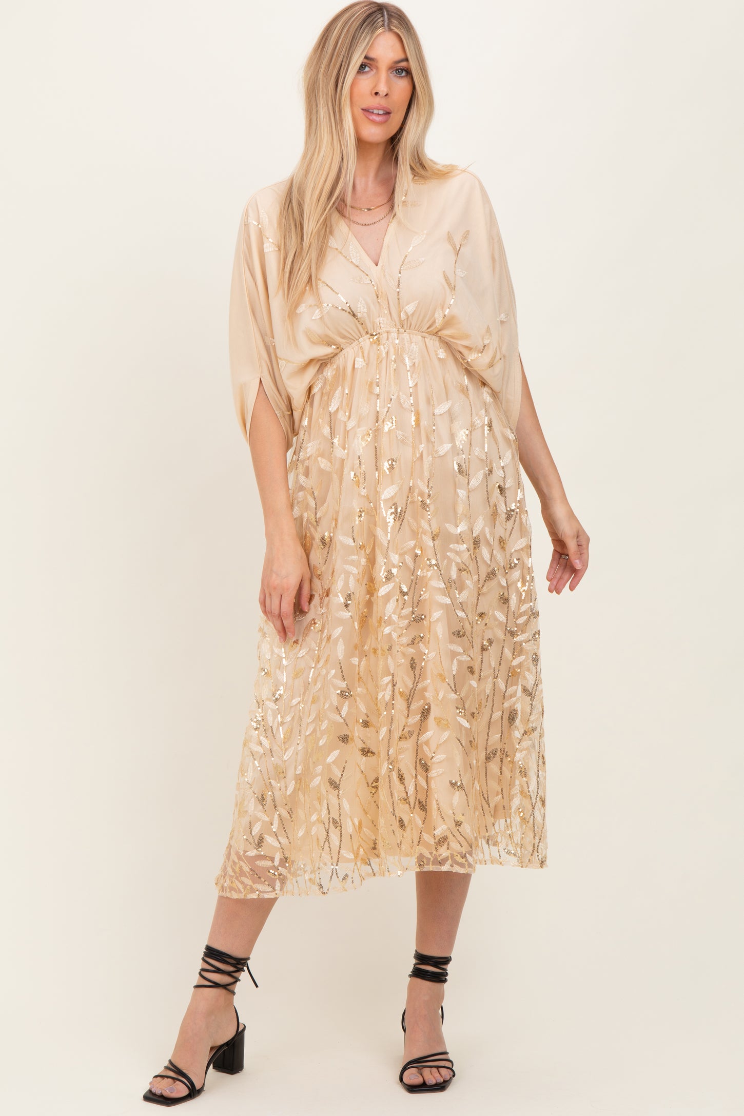 woman wearing a gold embroidered maxi dress with flutter sleeves and a cinched waist, standing in casual pose