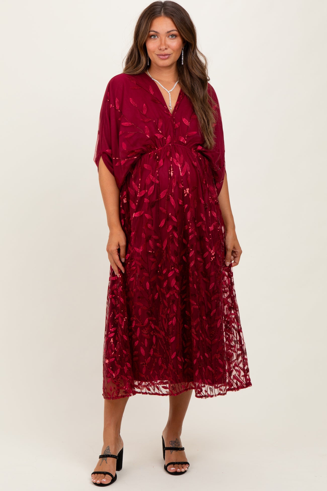 woman wearing a burgundy maternity dress with floral embroidery and a flowy silhouette, showcasing a baby bump