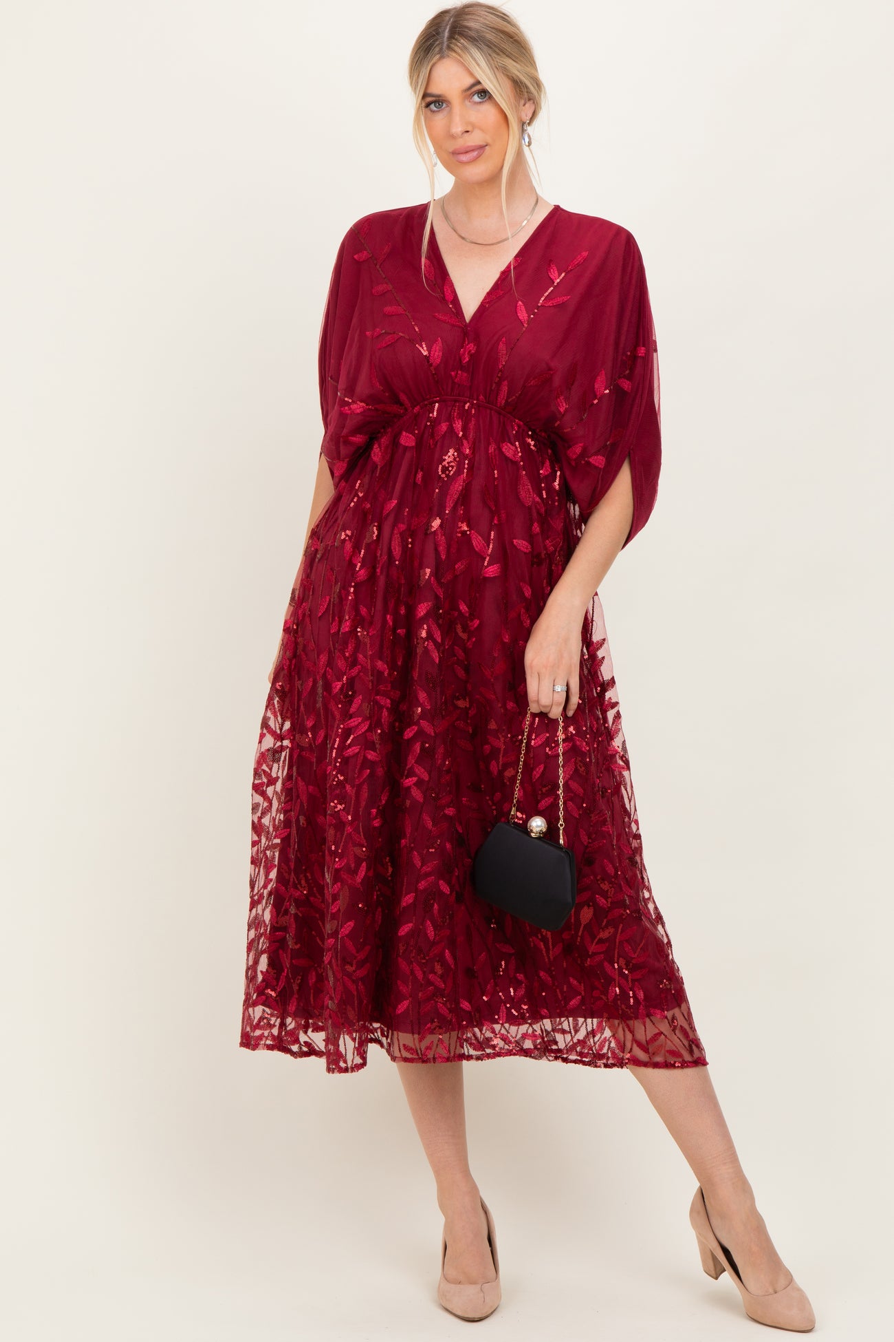 woman wearing a burgundy embroidered midi dress with a v-neck and batwing sleeves, holding a small black handbag
