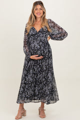 woman wearing a floral maternity maxi dress with long sheer sleeves and holding her baby bump