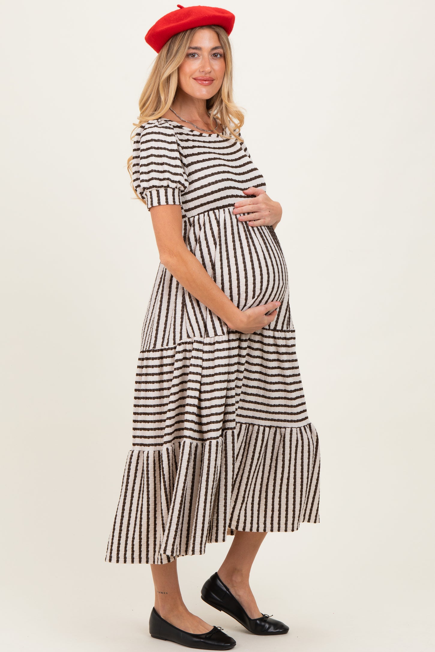 woman wearing a black and white striped maternity dress, smiling and holding her baby bump
