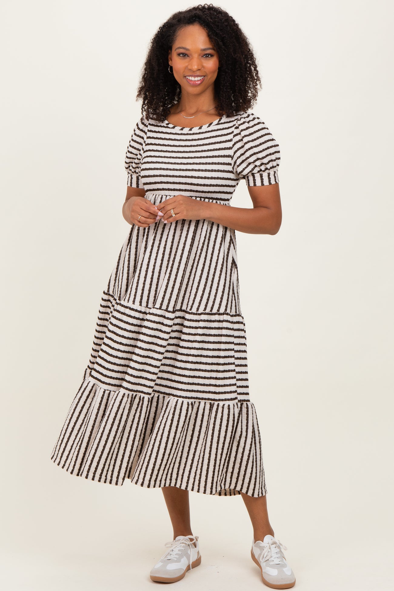 woman wearing a black and white striped tiered midi dress with short puff sleeves and white sneakers