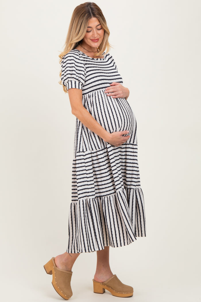 woman wearing a black and white striped maternity dress with short sleeves and a tiered skirt, holding her baby bump