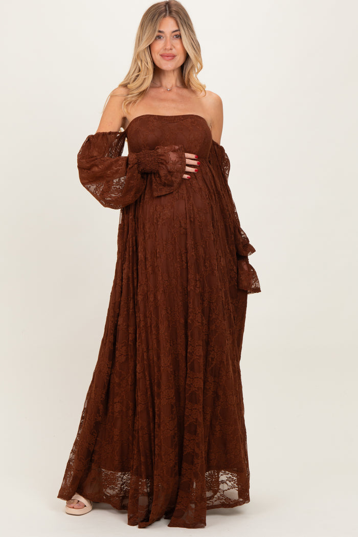 woman wearing a brown lace off-the-shoulder maxi maternity dress, cradling her baby bump