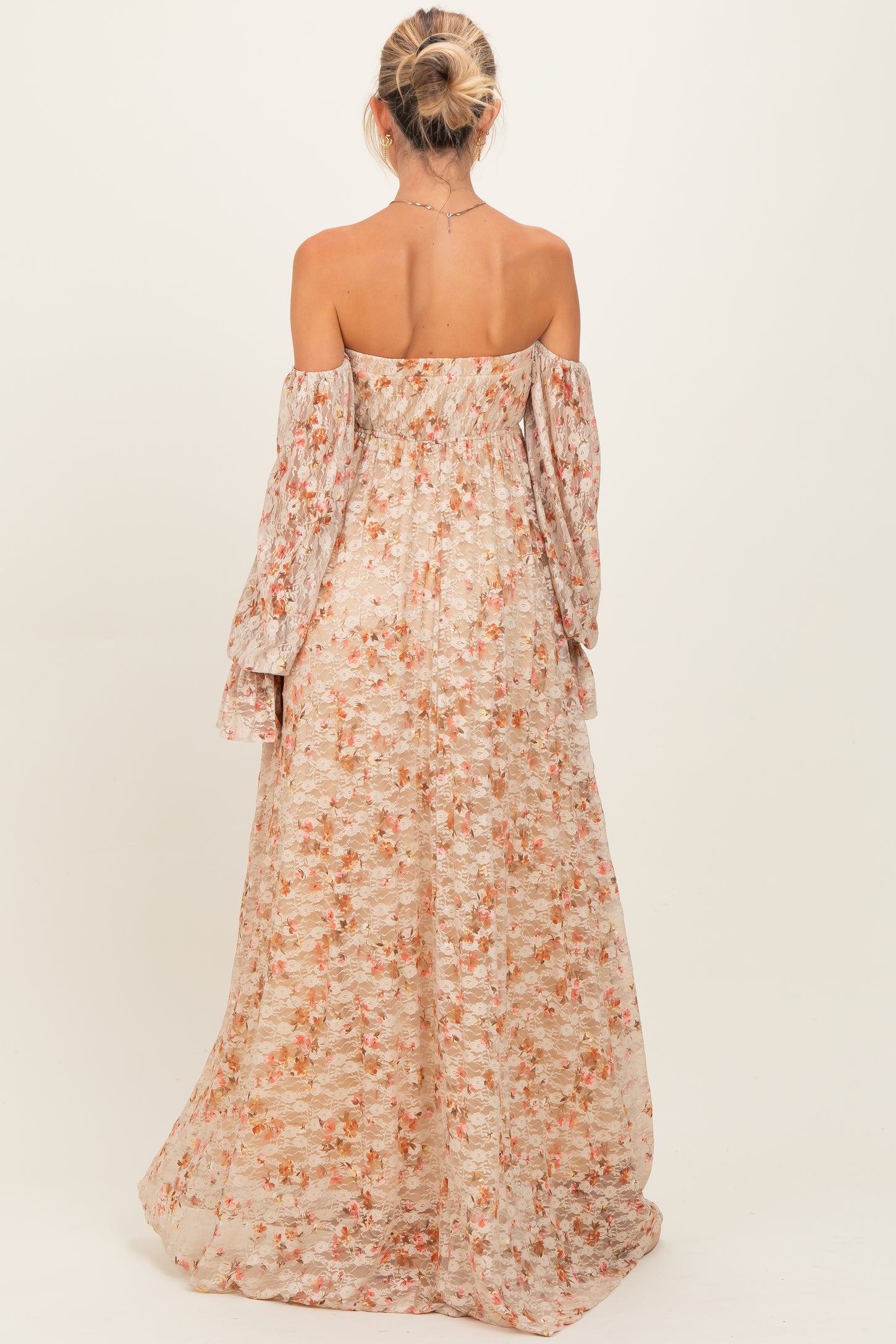 woman wearing a floral off-shoulder maternity maxi dress with long sleeves and a flowing skirt, showing a baby bump from behind