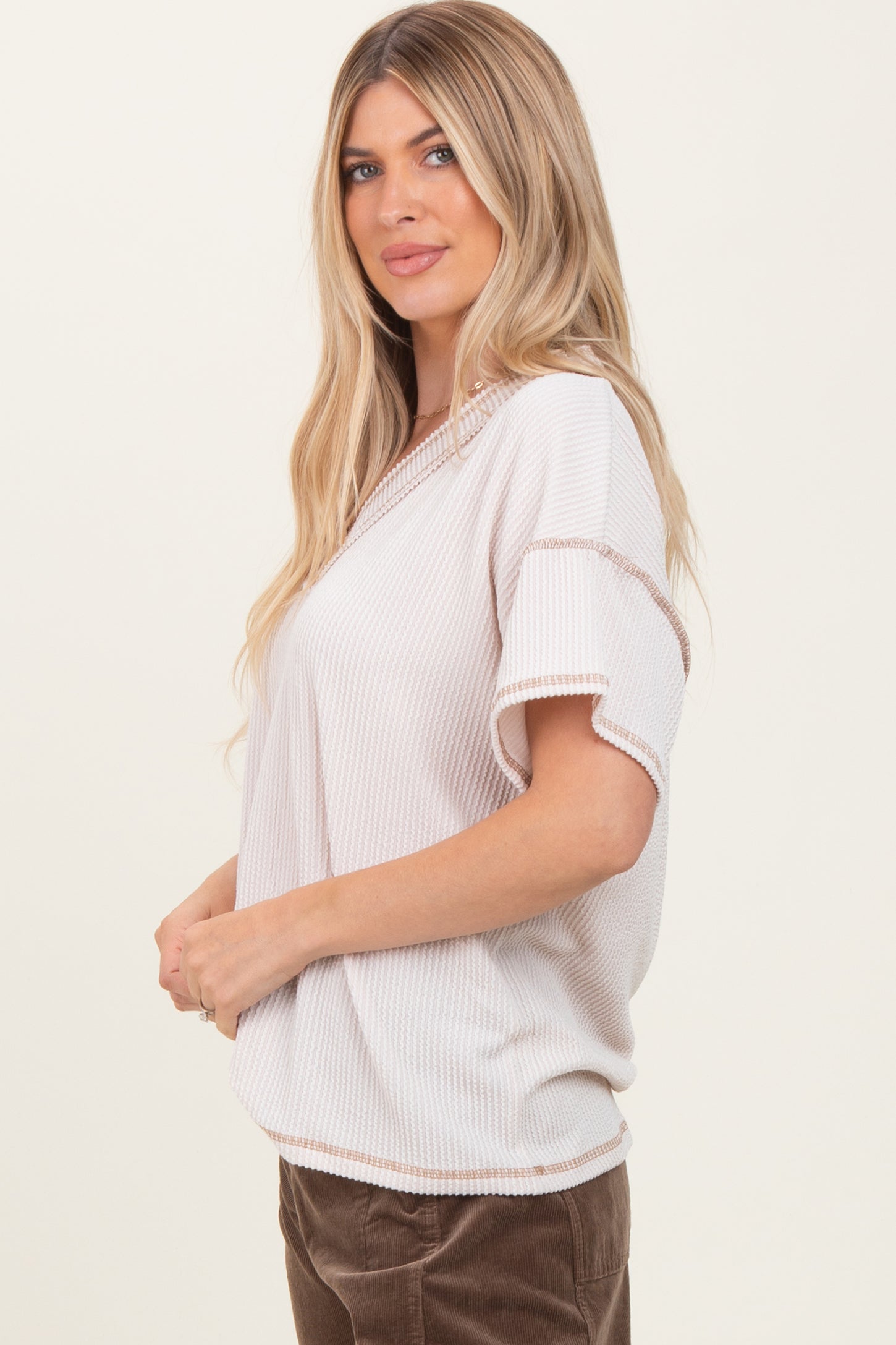 woman wearing a beige short sleeve top with ribbed texture and contrasting trim, styled with brown corduroy pants