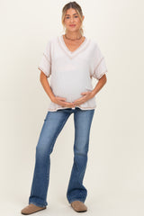 woman wearing a pink striped maternity top and blue flared jeans, holding her baby bump