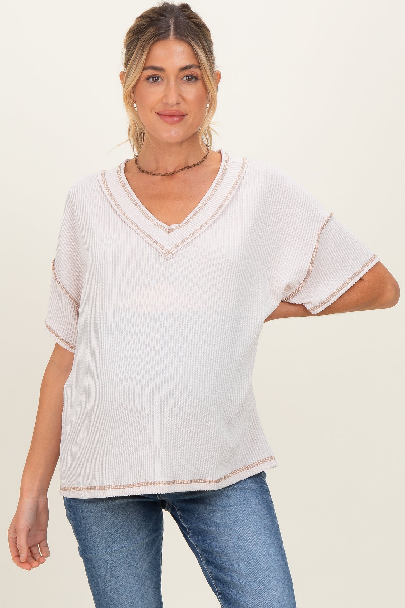 woman wearing a light pink maternity top with a v-neck and short sleeves, posing with a slight baby bump and casual jeans