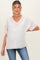 woman wearing a light pink maternity top with a v-neck and short sleeves, posing with a slight baby bump and casual jeans