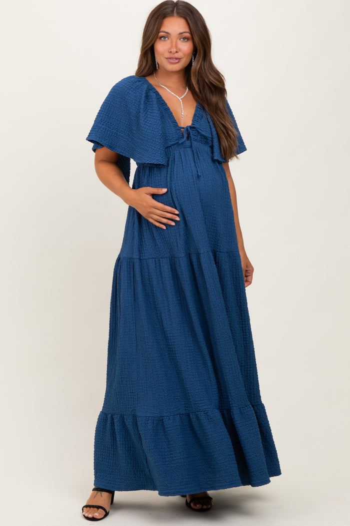 woman wearing a navy blue maternity maxi dress with tiered ruffles and a bow detail, holding her baby bump