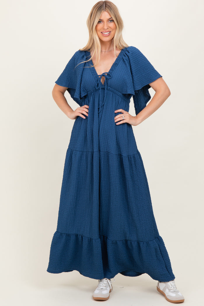 woman wearing a navy blue tiered maxi dress with flutter sleeves and a front tie detail