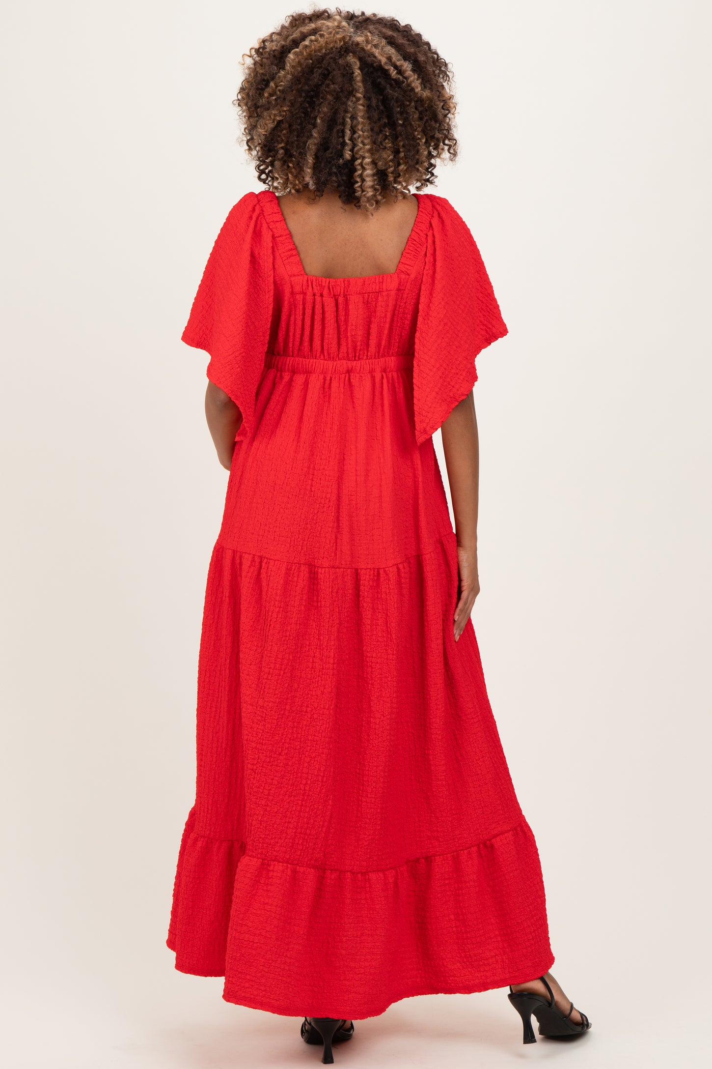 woman wearing a red flutter sleeve maternity maxi dress with a tiered design and a square neckline