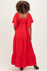 woman wearing a red flutter sleeve maternity maxi dress with a tiered design and a square neckline